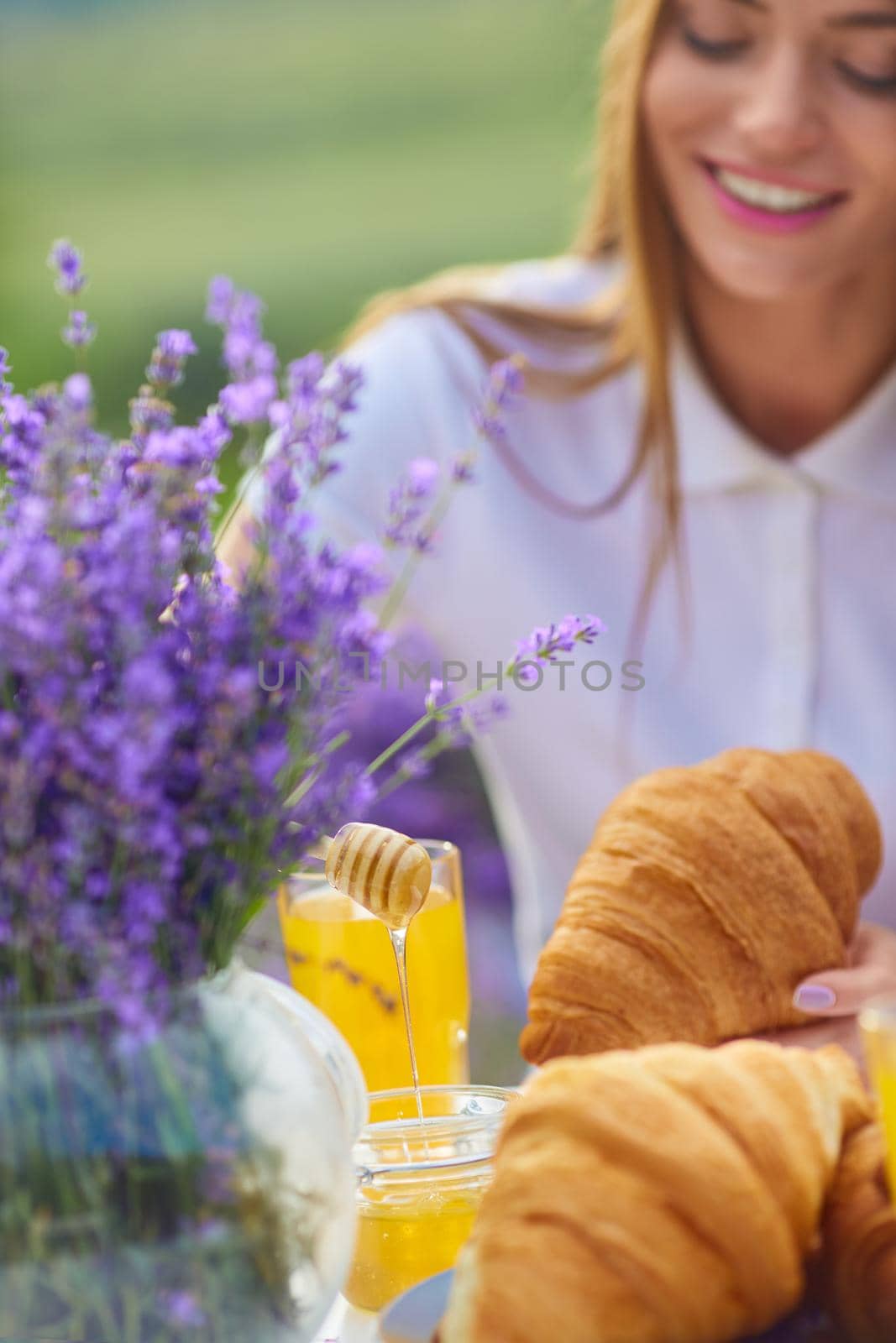 Smiling woman putting honey on croissants in lavender field. by SerhiiBobyk