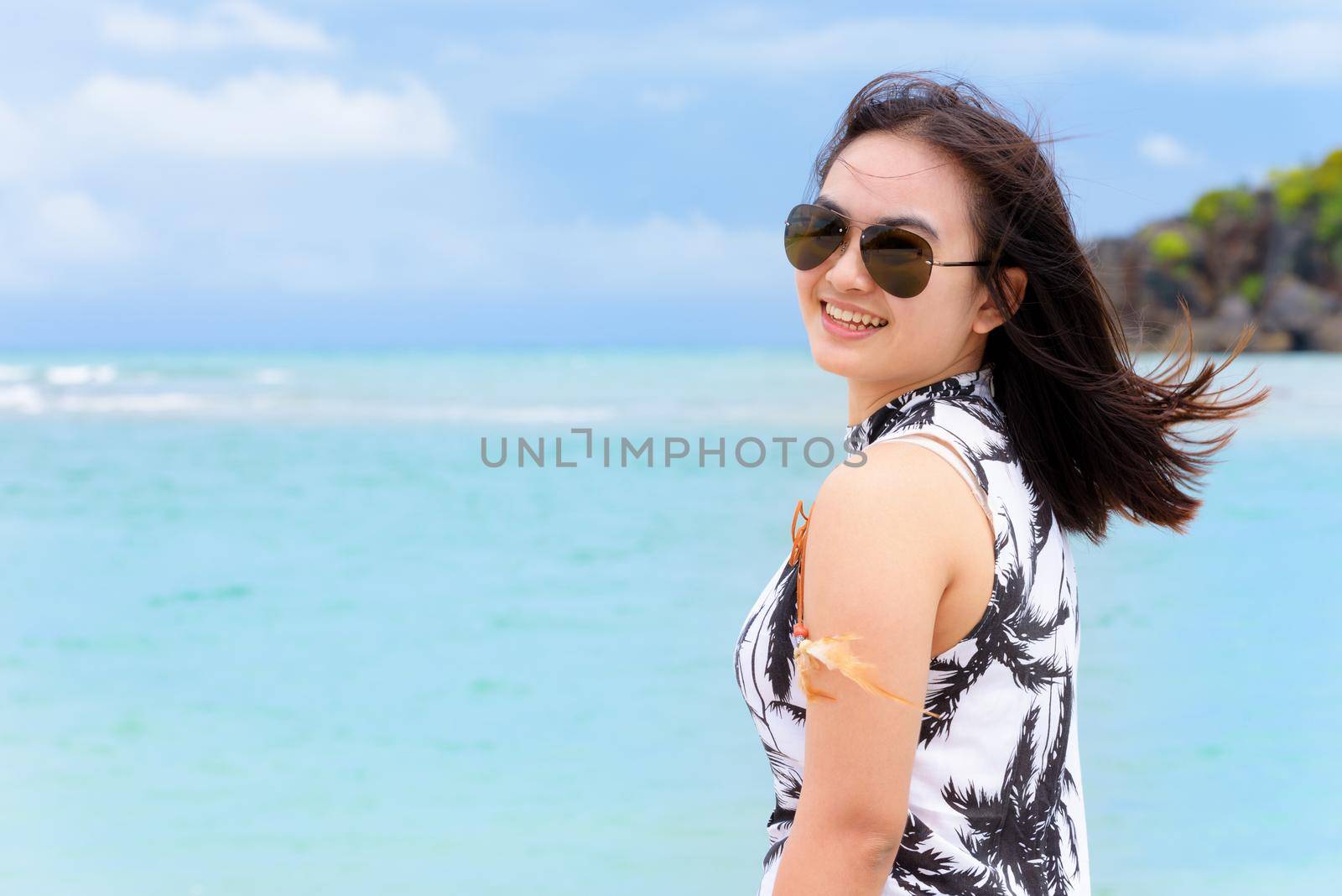 Beautiful woman tourist wearing sunglasse looking at the camera and smiling with happy on the beach and sea in summer sky background at Koh Tarutao island, Satun, Thailand