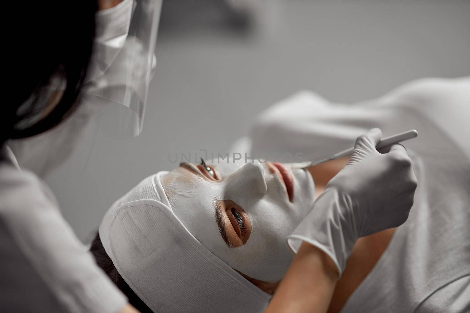 Side view close up of young attractive woman doing peeling for face in beautician. Concept of special beauty procedure for improvements skin with different mask for face.
