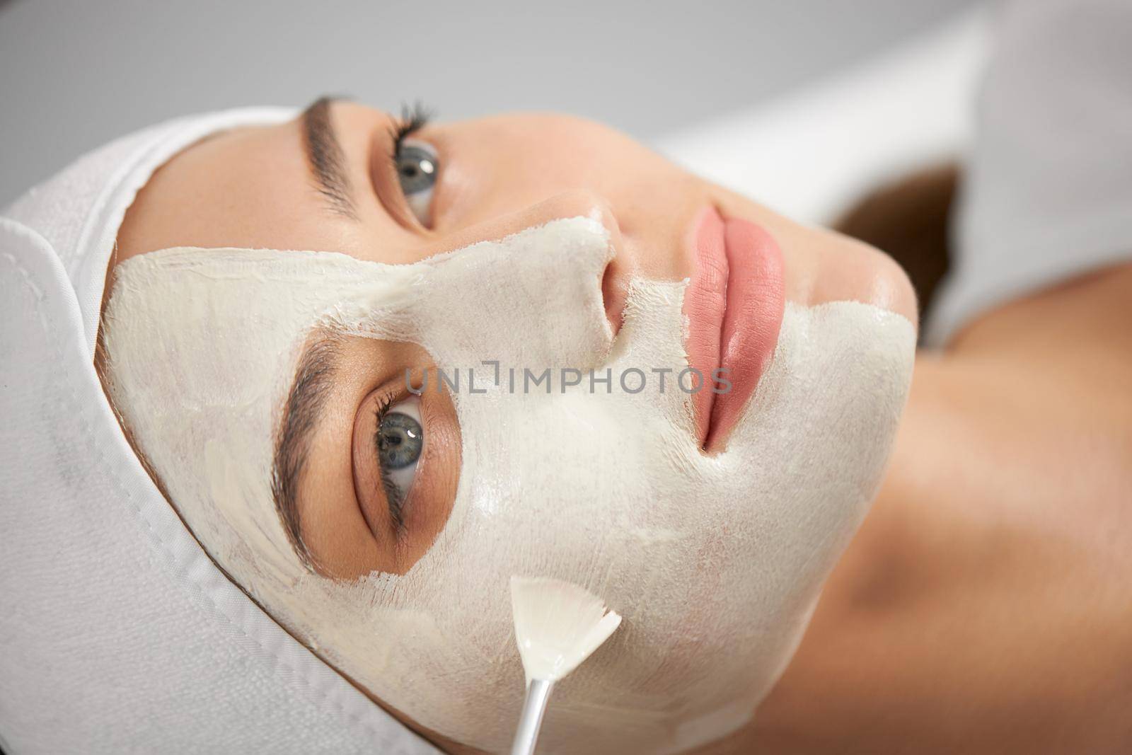 Side view close up of smiling young attractive woman lying on sofa in beautician. Concept of process procedure for improvements and rejuvenation skin in professional beauty salon.