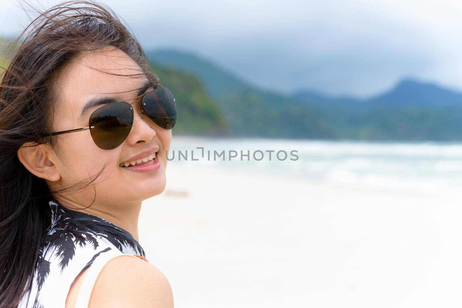 Close-up face beautiful woman tourist wearing sunglasse looking at the camera and smiling with happy on the beach and sea in summer at Tarutao island, Satun, Thailand