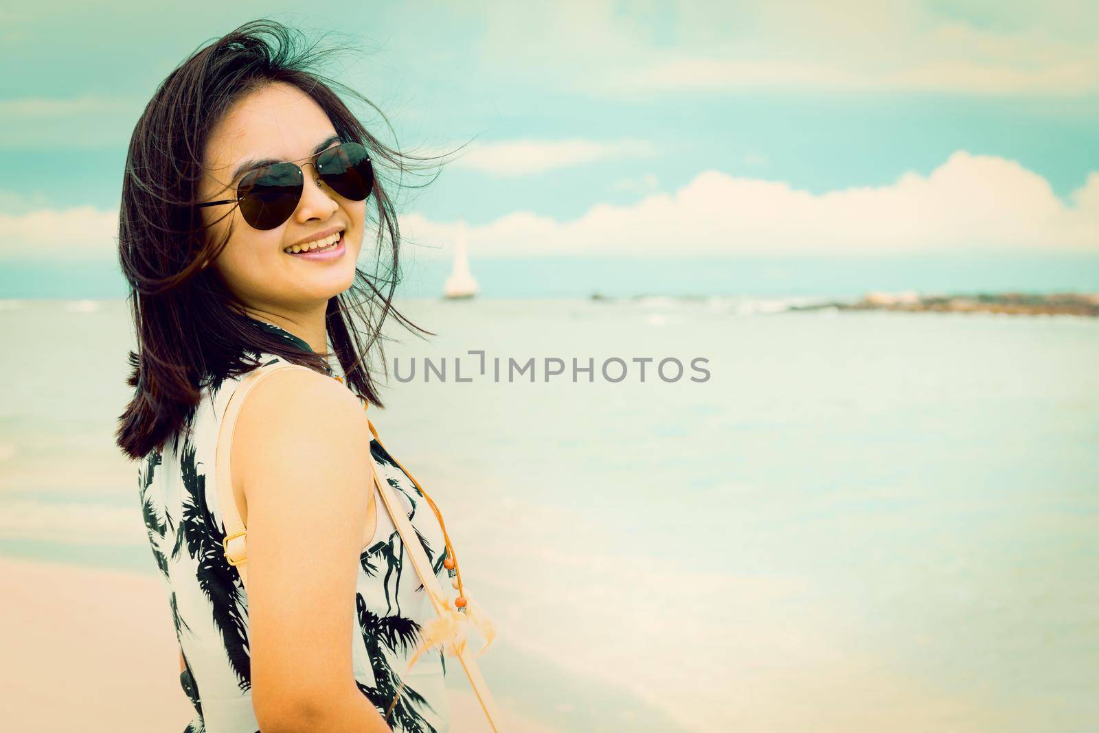 Beautiful woman tourist wearing sunglasse smiling looking at the camera on the beach near the sea at Tarutao island National Park, Satun, Thailand, in green teal and orang color vintage style