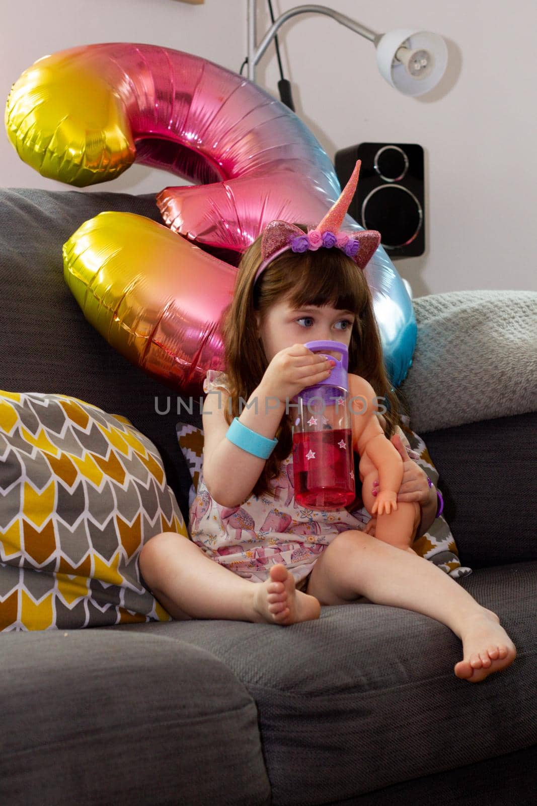 A Cute Baby Girl Sitting On A Sofa With A Colourful Balloon And A Doll by AlbertoPascual