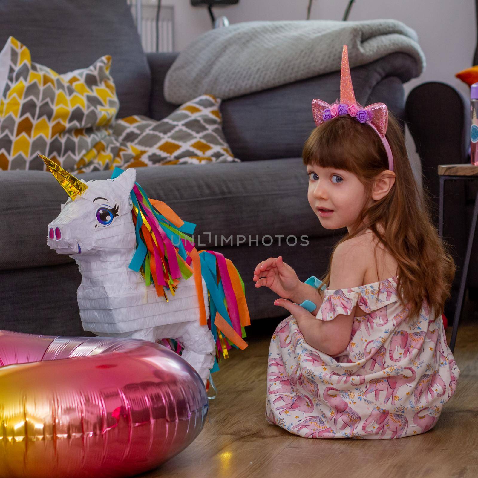 A Cute Baby Girl Sitting On The Floor With a Balloon And An Unicorn Pinata