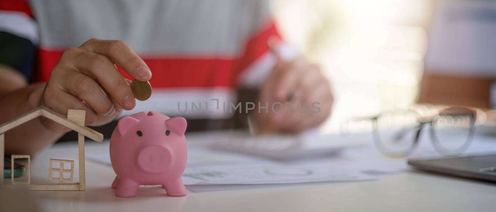 Close up of man putting coins in a piggy bank and calculating with calculator for saving money and financial home loan concept