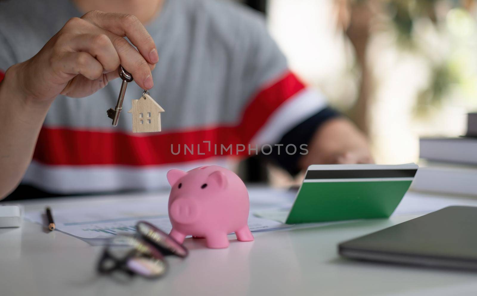 Saving money for first house or home mortgage loan concept, Man holding wooden house key chain with white piggy bank on wooden table with copy space, real estate or property investment