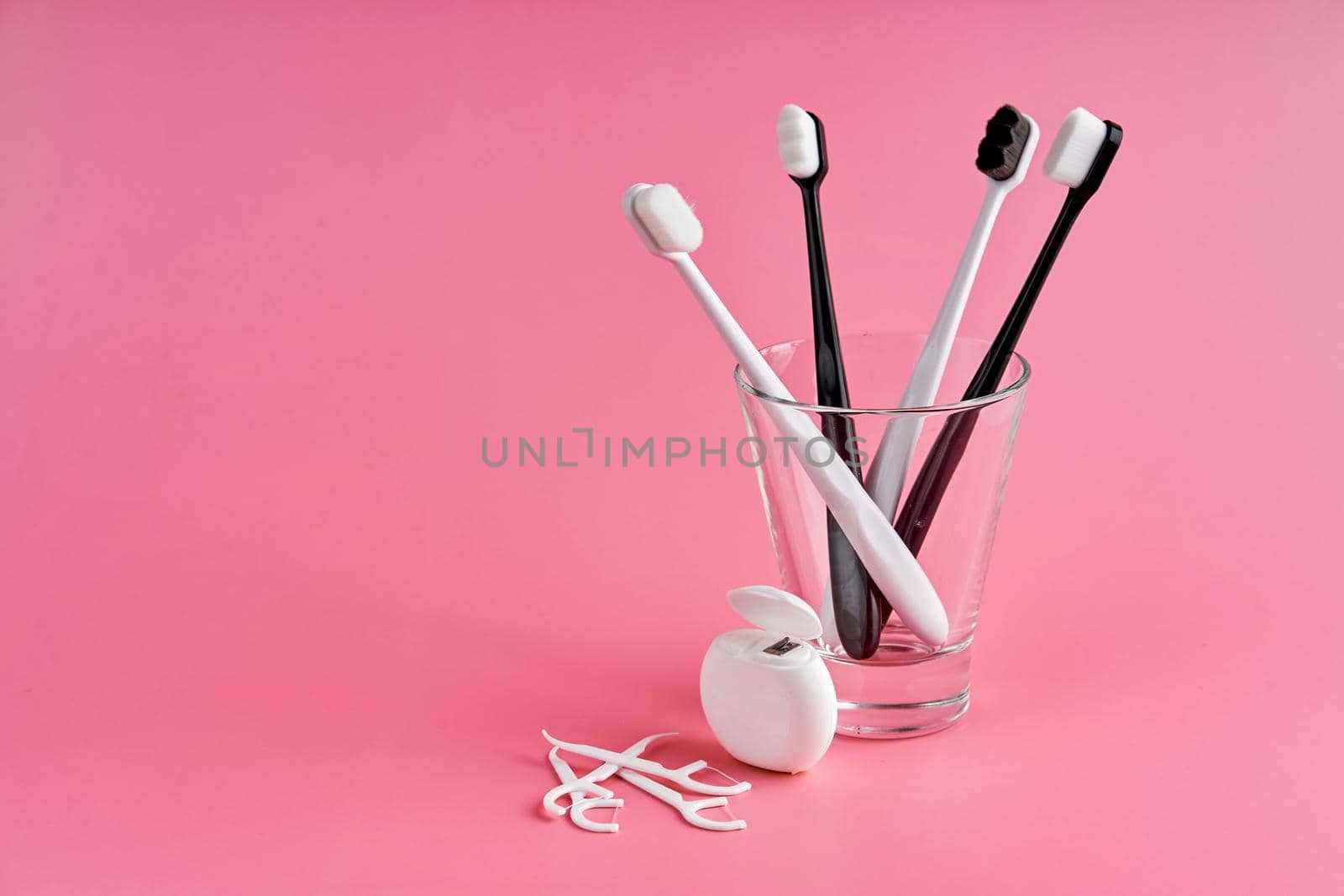 Fashionable toothbrush with soft bristles. Popular toothbrushes. Hygiene trends. Oral hygiene kit. Toothbrushes in glass, floss thread and toothpicks on a pink background by Try_my_best