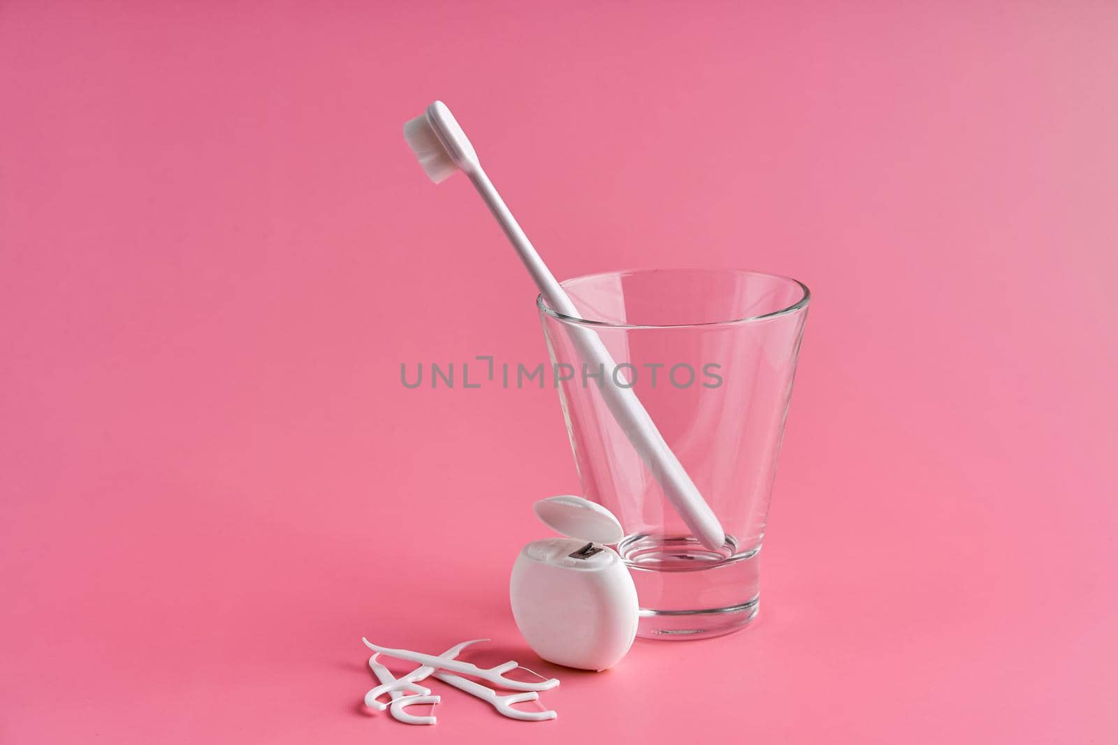 Fashionable toothbrush with soft bristles. Popular toothbrushes. Hygiene trends. Oral hygiene kit. Toothbrushes in glass, floss thread and toothpicks on a pink background.