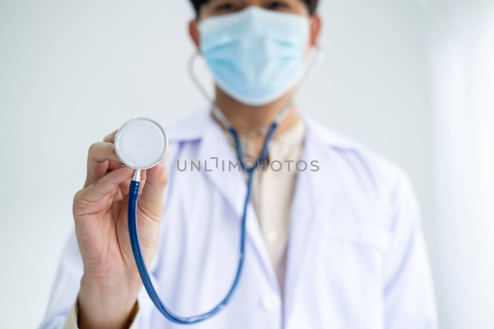 Young man doctor holding stethoscope and medical mask to protect against coronavirus 2019 disease or COVID-19 global outbreak.
