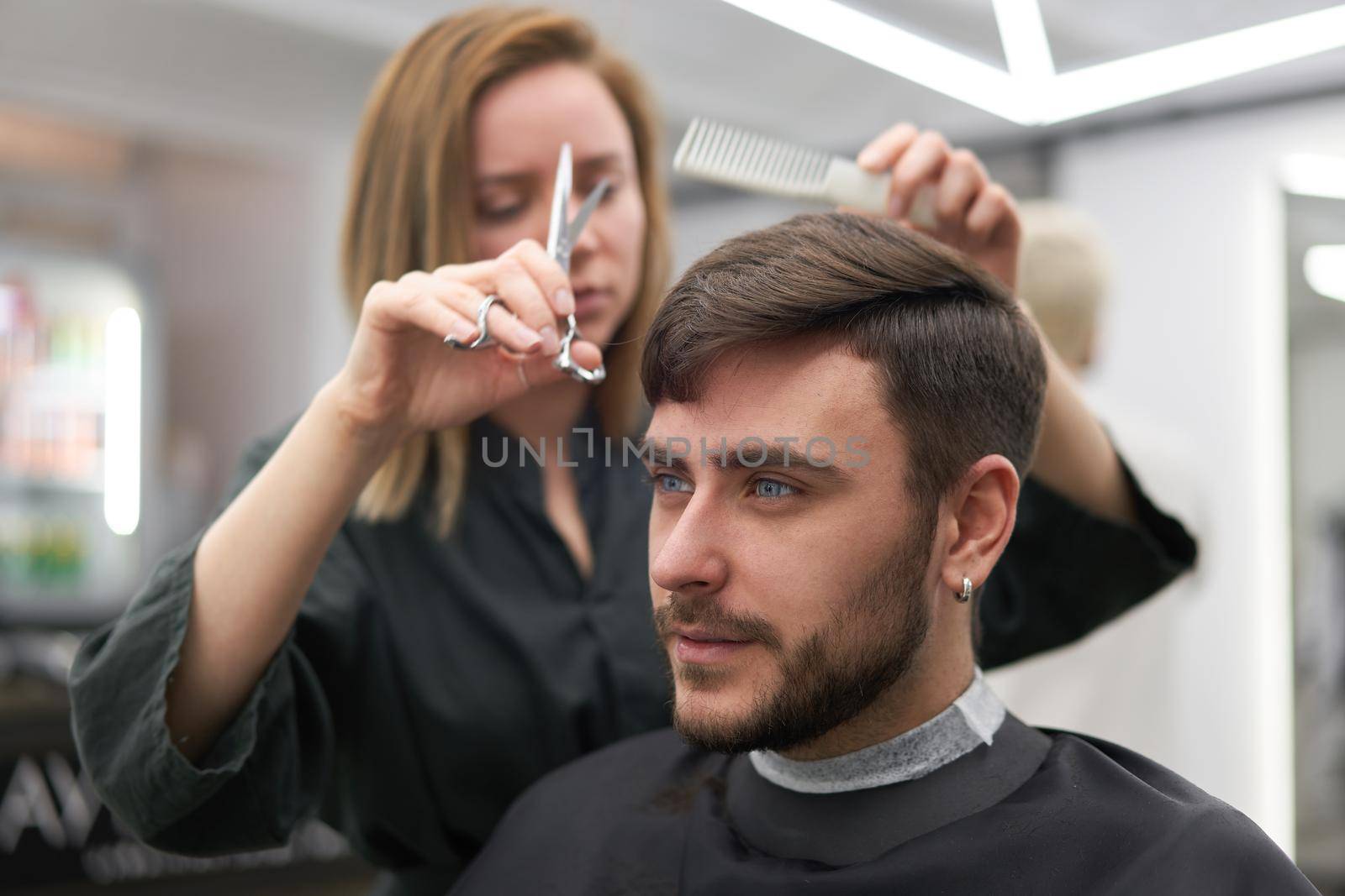 Stylish man sitting barber shop Hairstylist Hairdresser Woman cutting his hair Portrait handsome happy young bearded caucasian guy getting trendy haircut Attractive barber girl working serving client