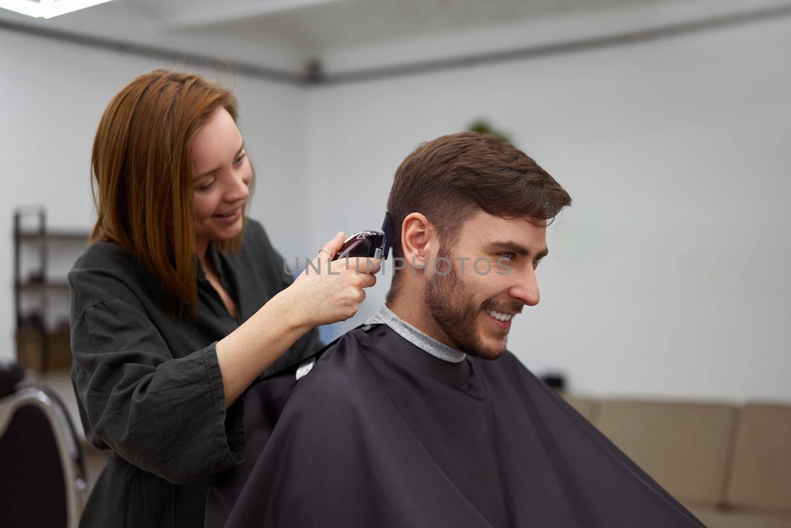 Stylish man sitting barber shop Hairstylist Hairdresser Woman cutting his hair Portrait handsome happy young bearded caucasian guy getting trendy haircut Attractive barber girl working serving client