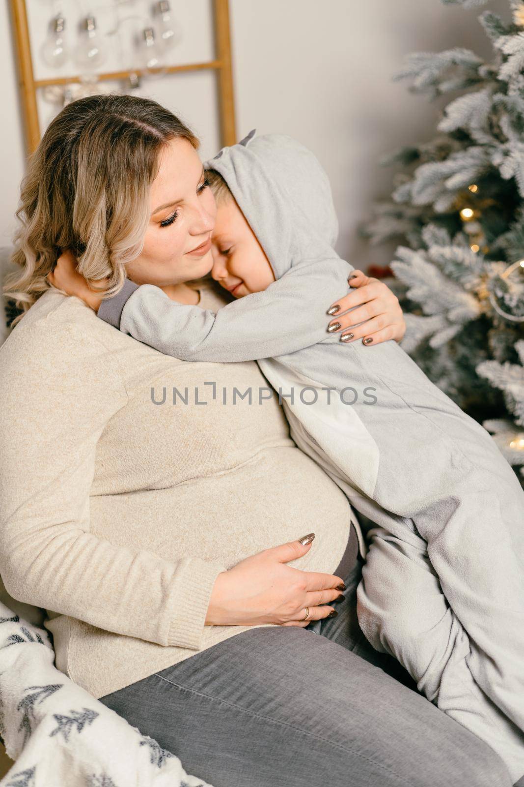 Mom plays with child. Happy family Portrait In Home pregnant mother embraces his little son. Happy new year. decorated Christmas tree Christmas morning bright living room Caucasian woman with child