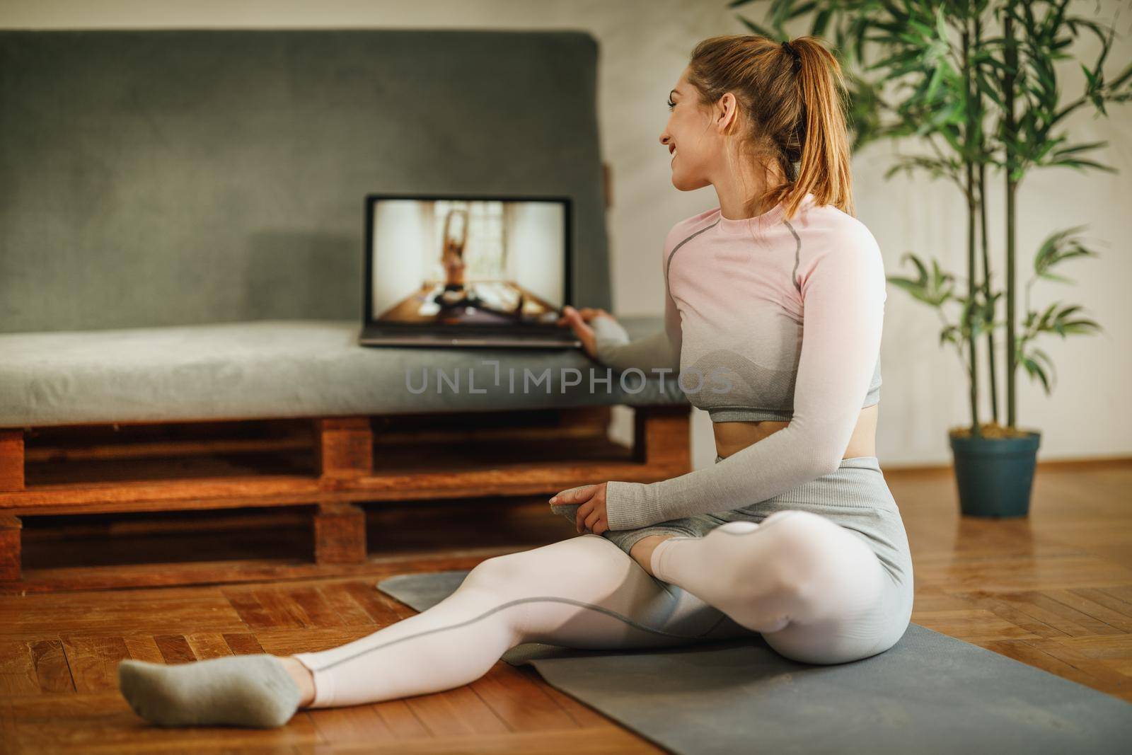 An attractive young woman sitting alone and stretching before a workout indoors.