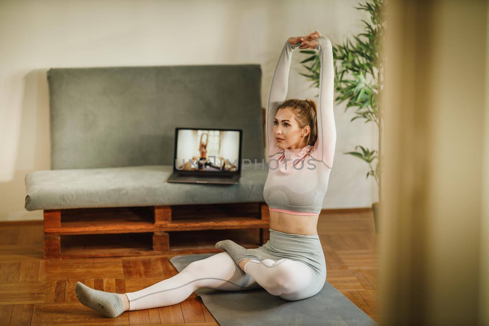 An attractive young woman sitting alone and stretching before a workout indoors.