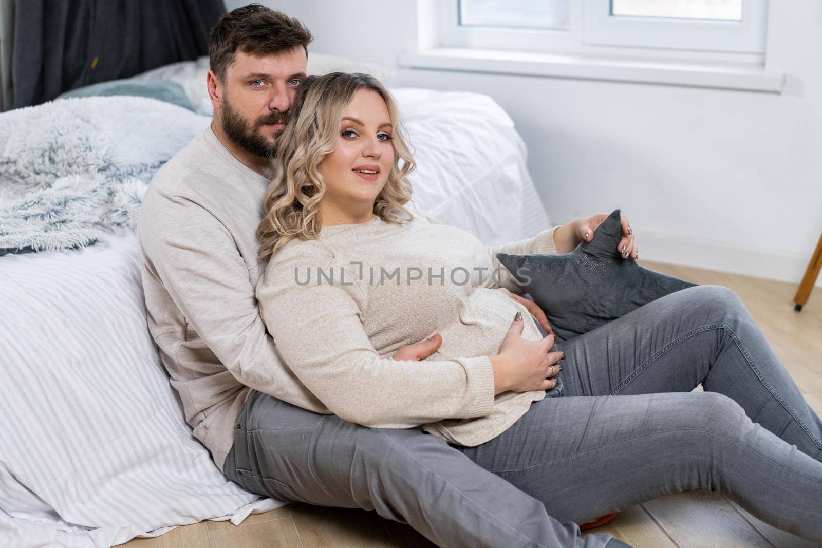 Happy family concept. Husband hug belly pregnant wife sitting floor indoor living room near sofa Caucasian man and woman pregnancy and new life concept. Love and care