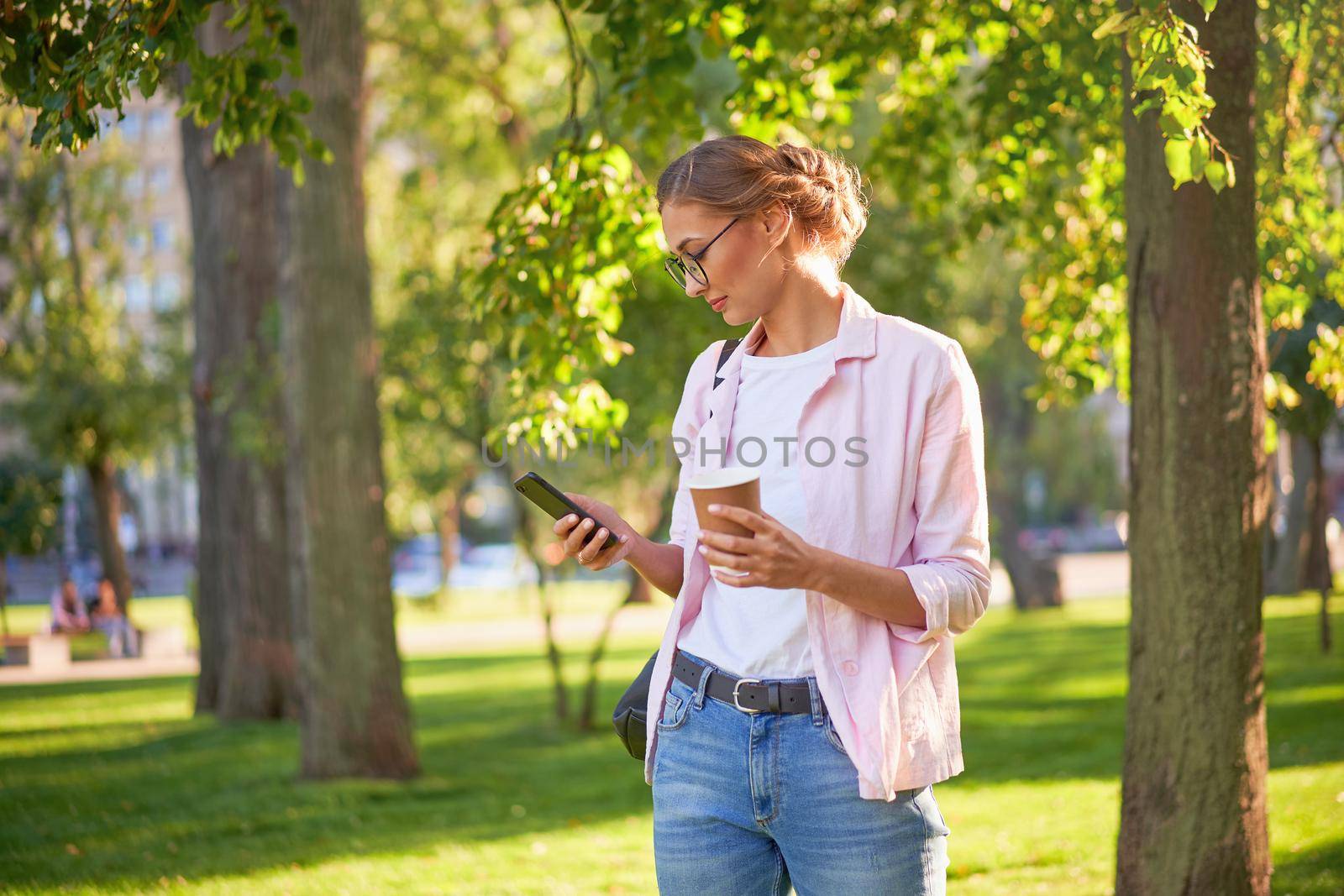 Businesswoman standing summer park Business person using smartphone Outdoors Successful european caucasian woman freelancer or teacher walking outside backpack dressed jeans white shirt pink jacket
