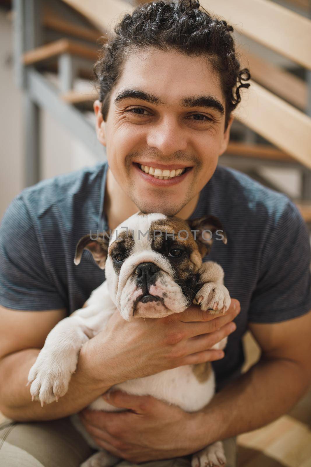 Portrait of a happy young man with his English bulldog puppy while moving into their new home. Looking at camera.