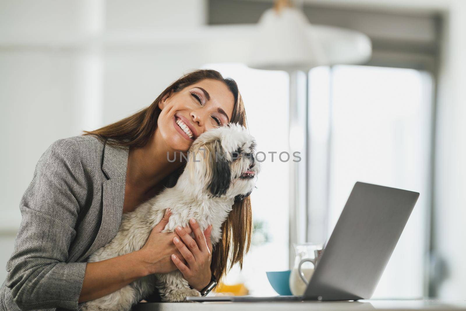 Young female freelancer sitting with her pet dog and using on her laptop during work from home.