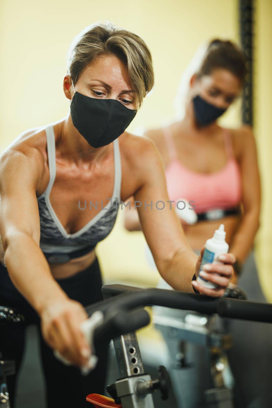 Shot of a muscular young woman with protective mask cleaning fitness gym equipment afther workout during Covid-19 pandemic.