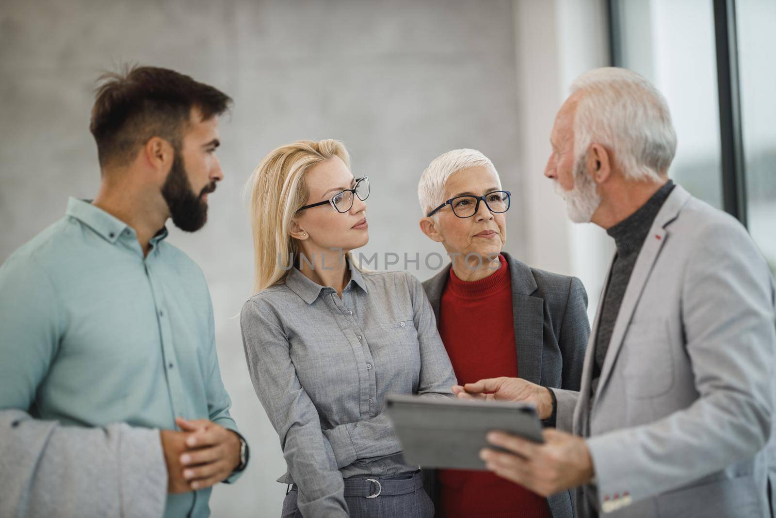 A group of confident business people using digital tablet  and having a discussion with each other during the meeting in a modern office.