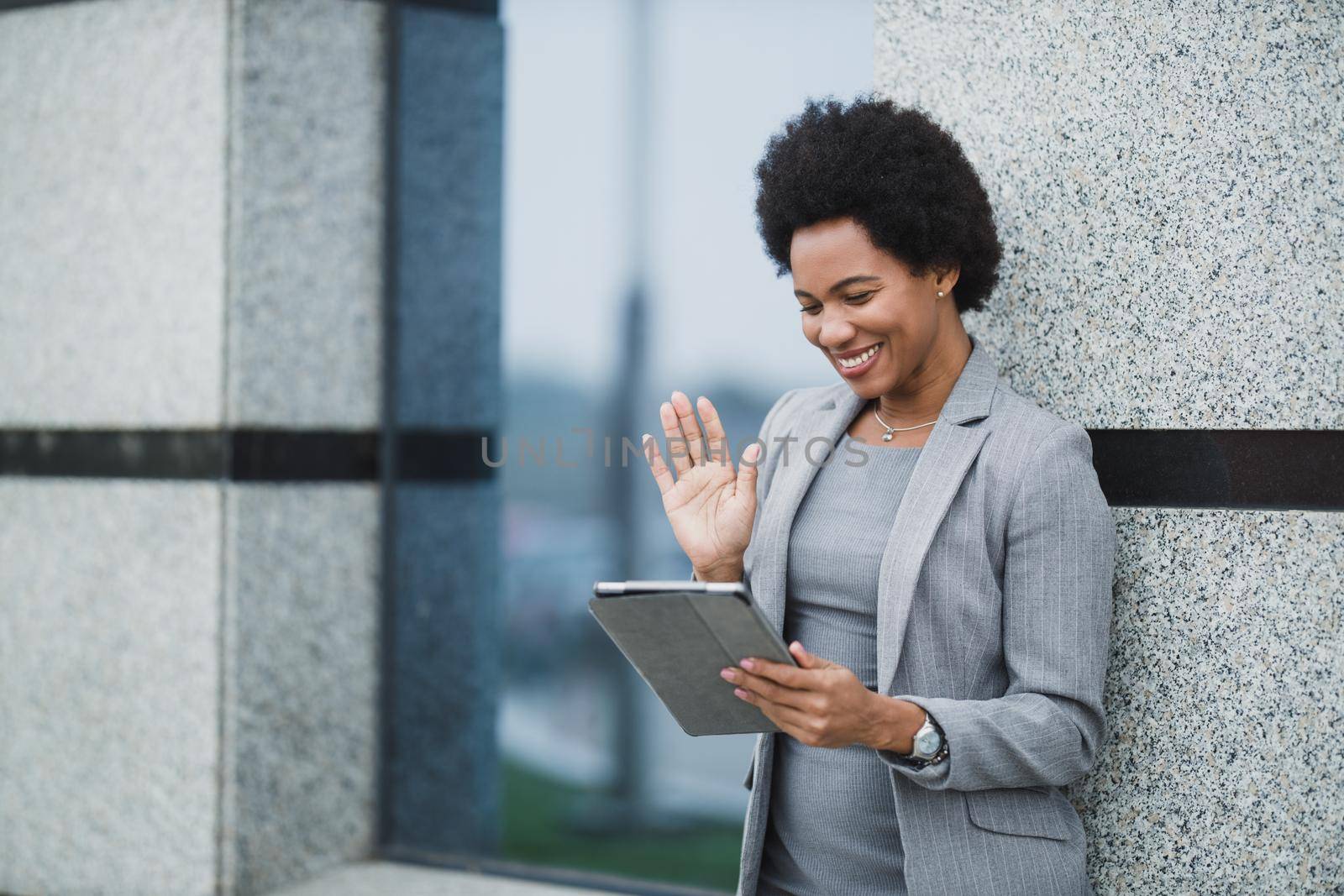Portrait of a cheerful black business woman making video call on a digital tablet in front a corporate building.