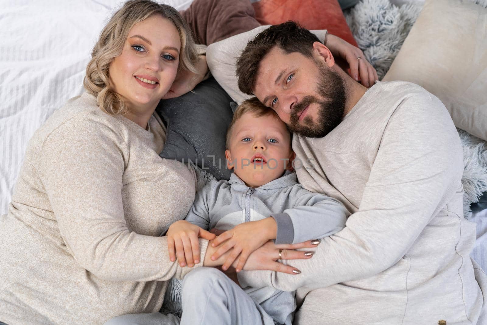 Happy family concept Mother father and little son have fun at home Caucasian family indoors Pregnant mom beard dad and funny little boy lie on the couch
