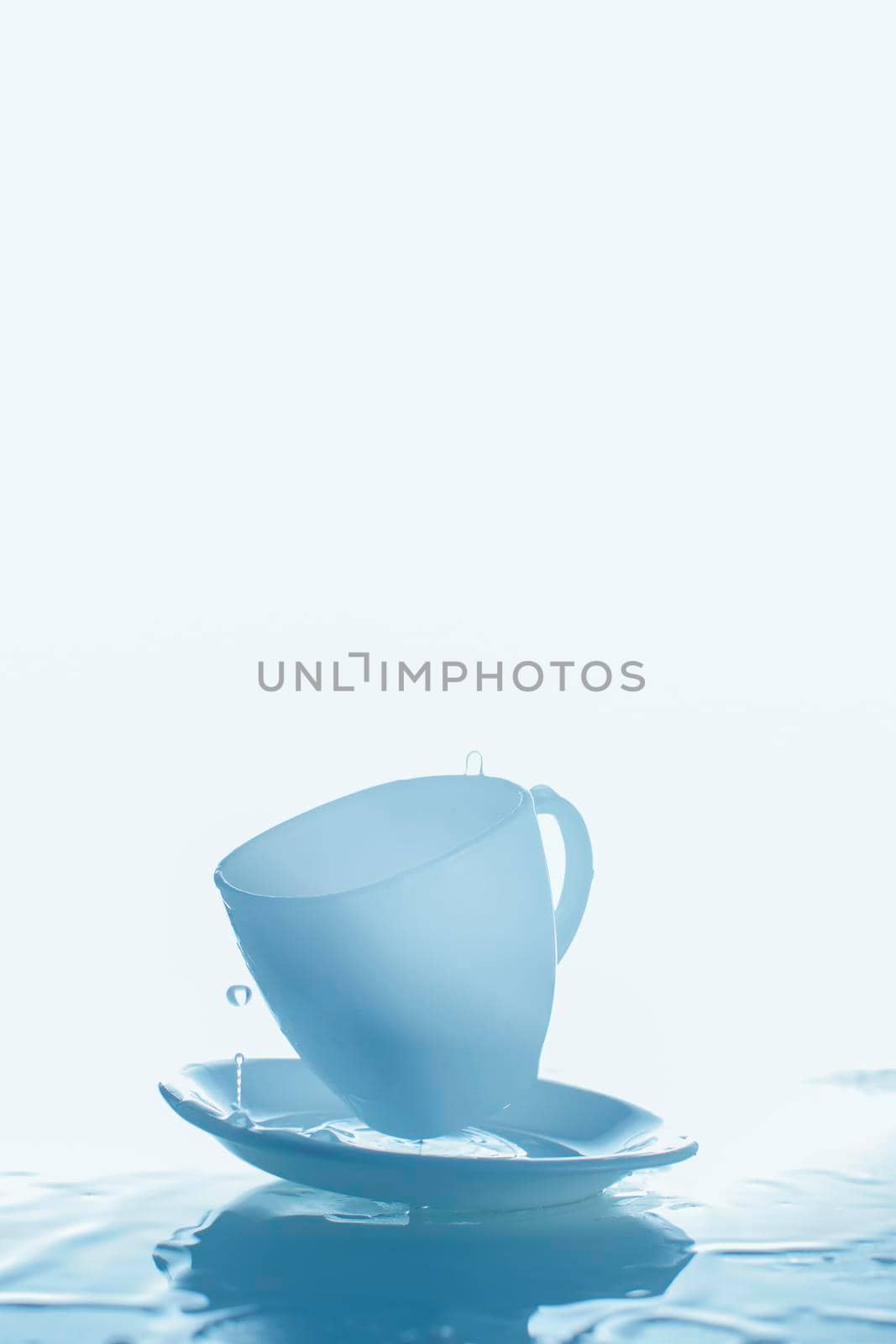 Blue cup and saucer with splashes of water.Vertical photograph of glass and water on a blue background.