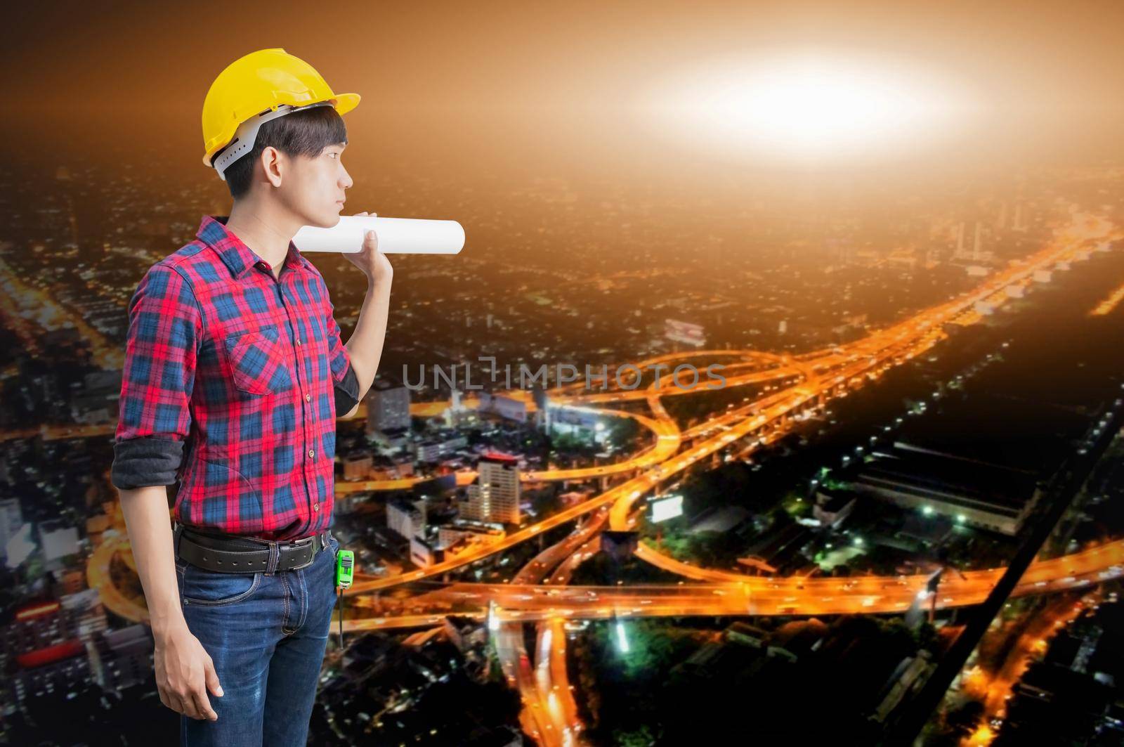Engineer holding rolled blueprints in construction concept with night cityscape Blurred background by pramot