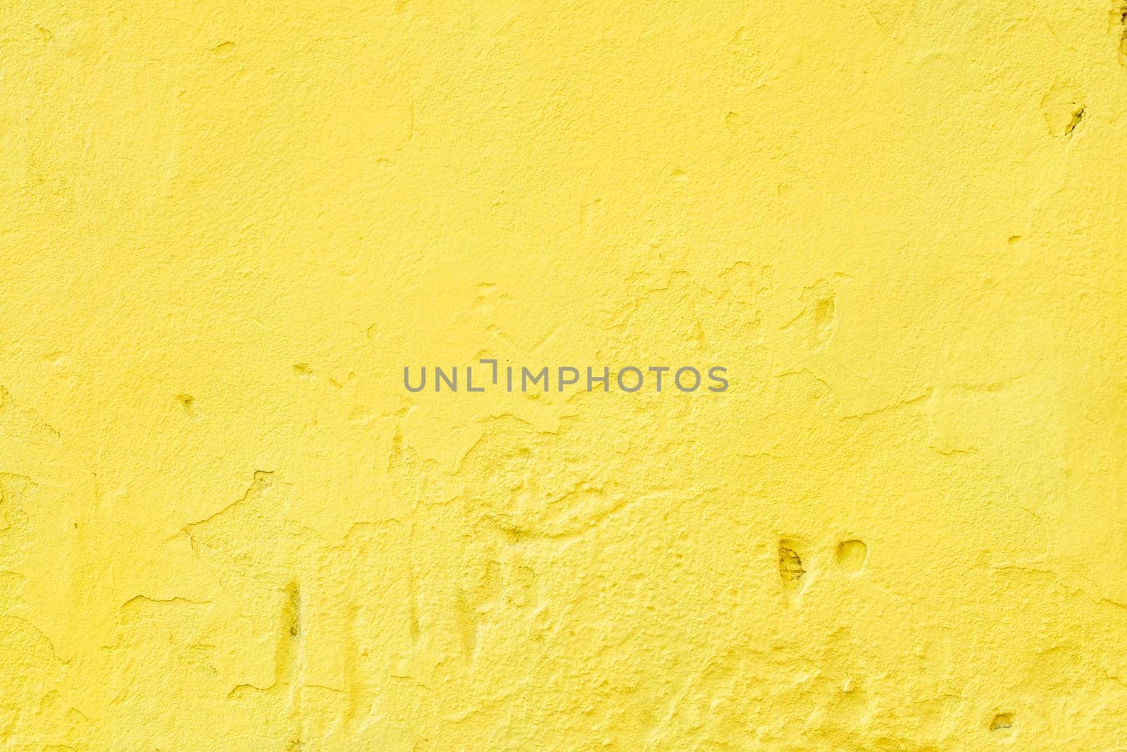 A close-up of a fragment of an old wall with rough, bright yellow plaster.