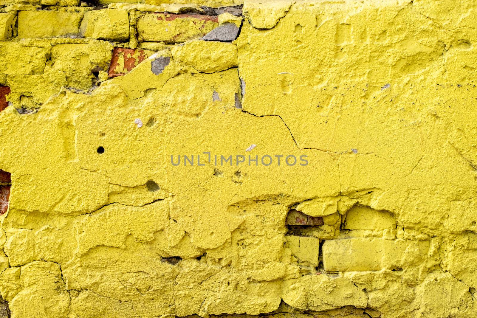 Close-up of a fragment of an old wall with rough plaster and bright yellow brickwork.