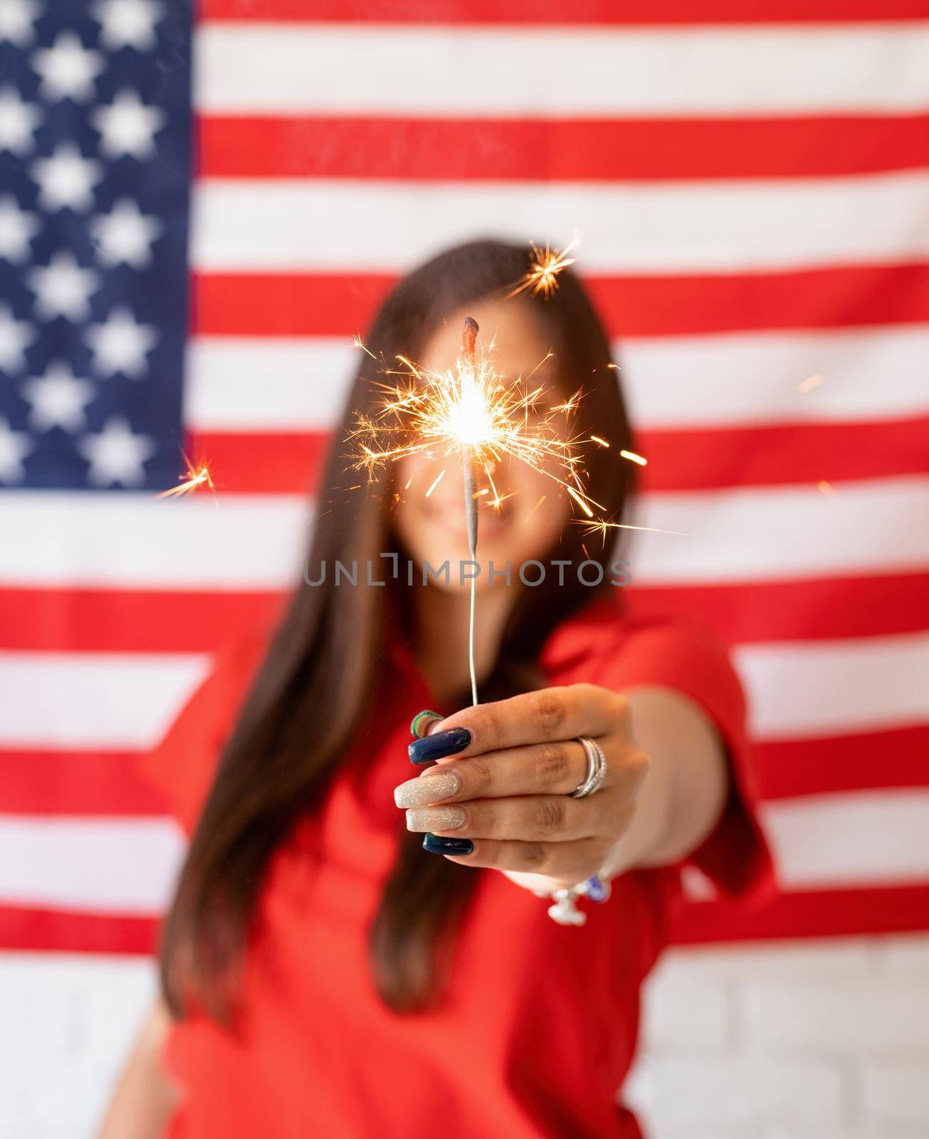 Independence day of the USA. Happy July 4th. Sparkling Bengal fire in caucasian woman hand. Beautiful woman holding a sparkler on US flag background