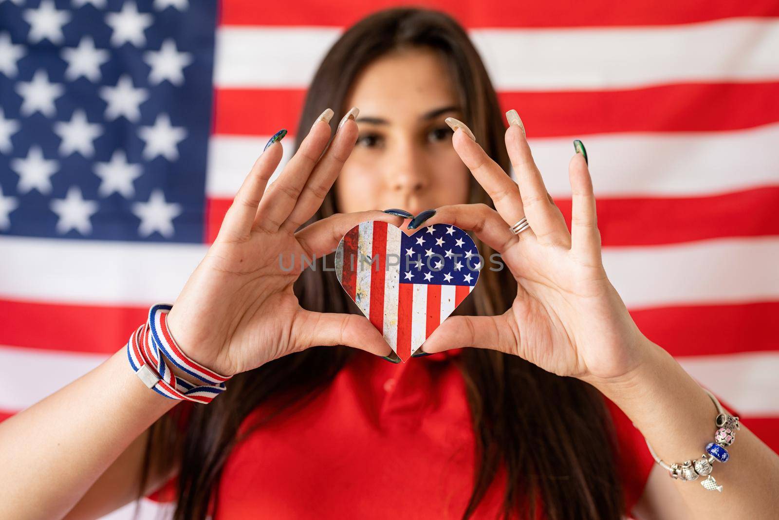 Independence day of the USA. Happy July 4th. Beautiful woman holding a heart shape national flag on the USA flag background