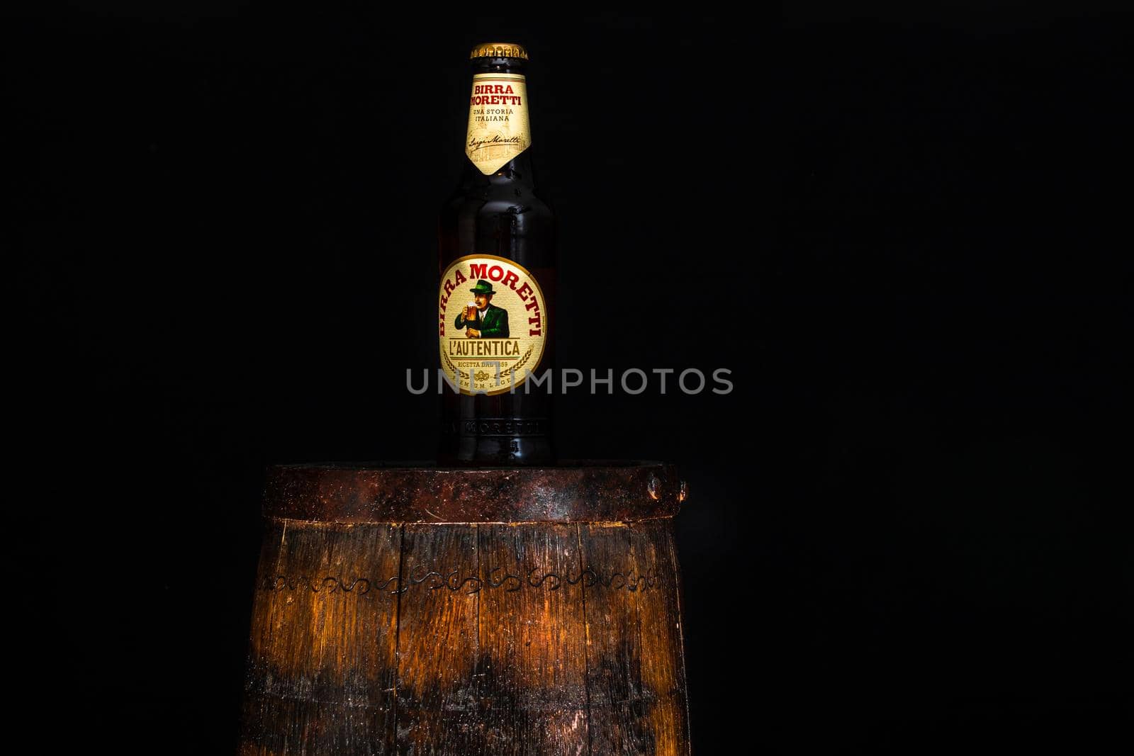 Bottle of Birra Moretti beer on wooden barrel with dark background. Illustrative editorial photo Bucharest, Romania, 2021 by vladispas