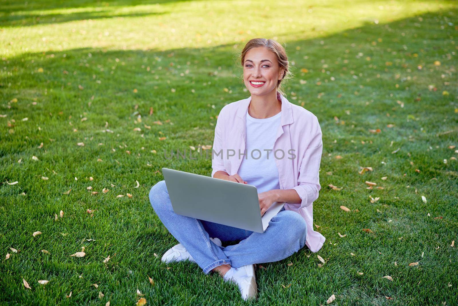 Businesswoman sitting grass summer park using laptop Business persone working remote. Outdoors Successful european caucasian woman freelancer make video call Combing her hair looking laptop screen.