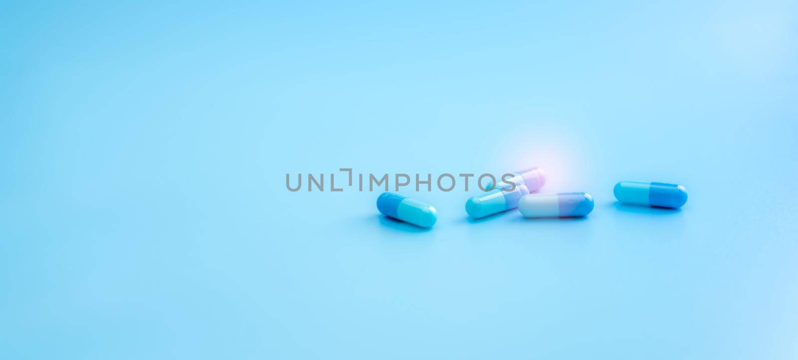 Blue capsule pills on blue background. Pharmacy shop banner. Healthcare and medicine. Pharmaceutical industry. Drug research and development for treatment coronavirus infection. Antiviral medicine. by Fahroni