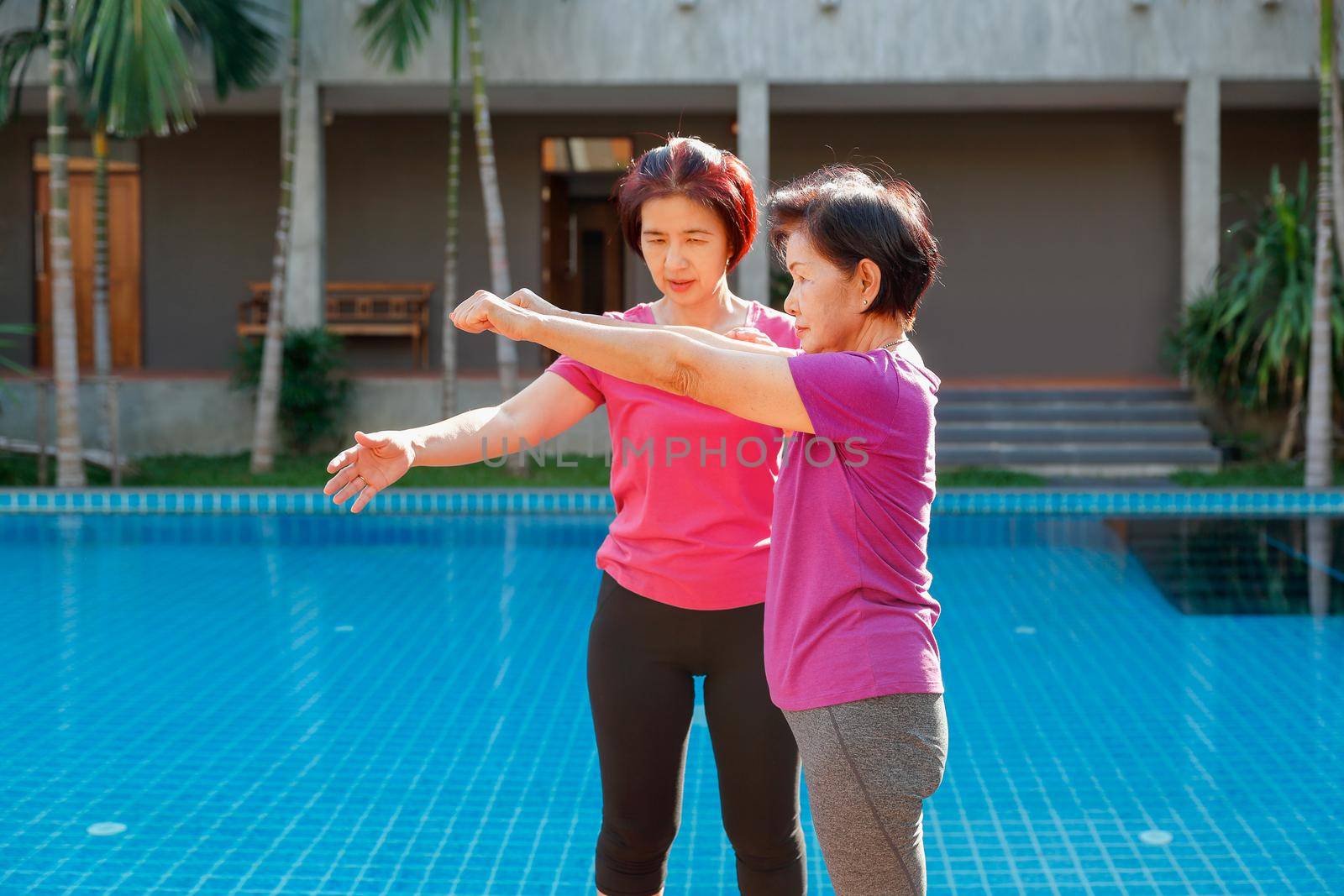 elderly woman doing exercise with daughter at pool patio