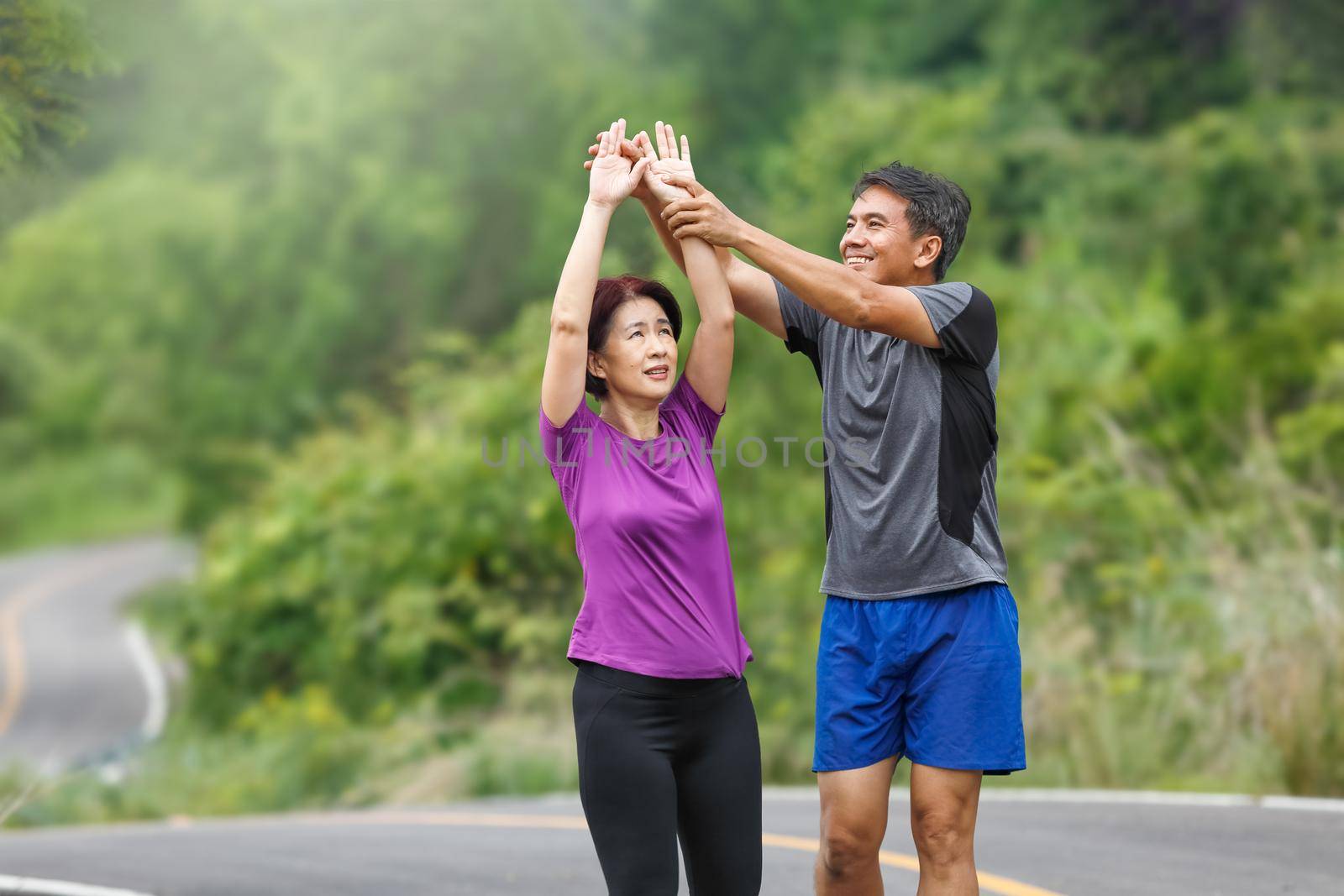 Asian middle aged couple stretching muscles before jogging in park by toa55