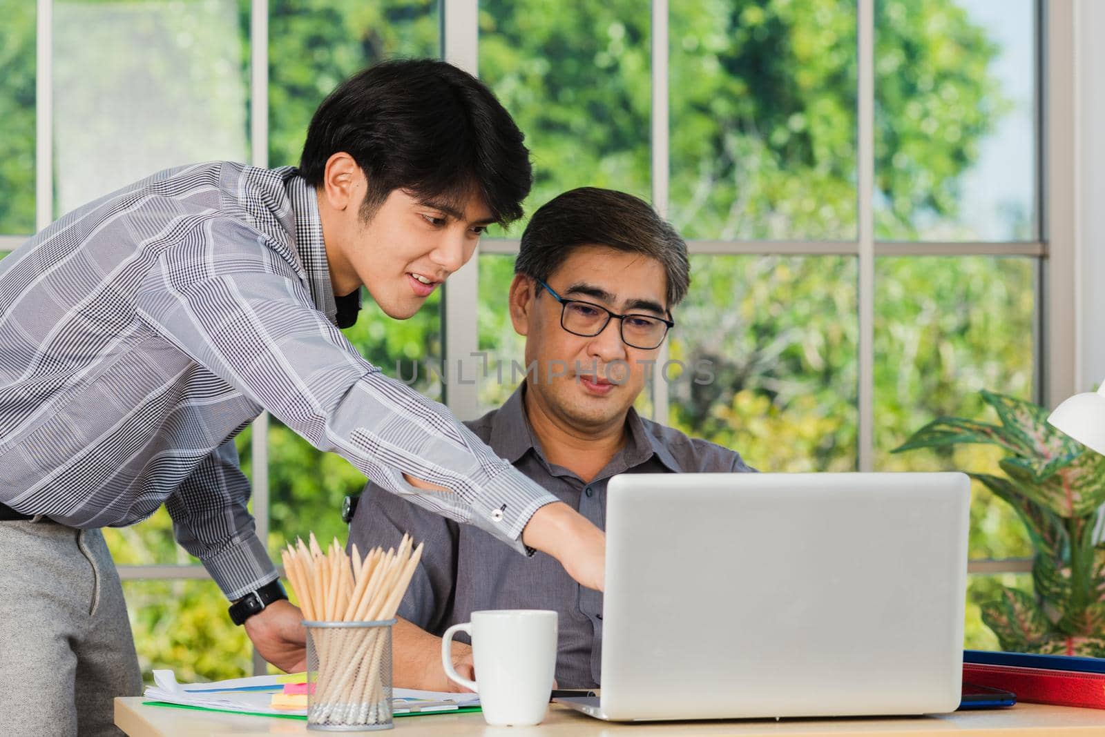 Asian senior and junior two businessmen discuss something during their meeting consultation project, Mature boss with a business partner working together on the laptop computer on desk home office