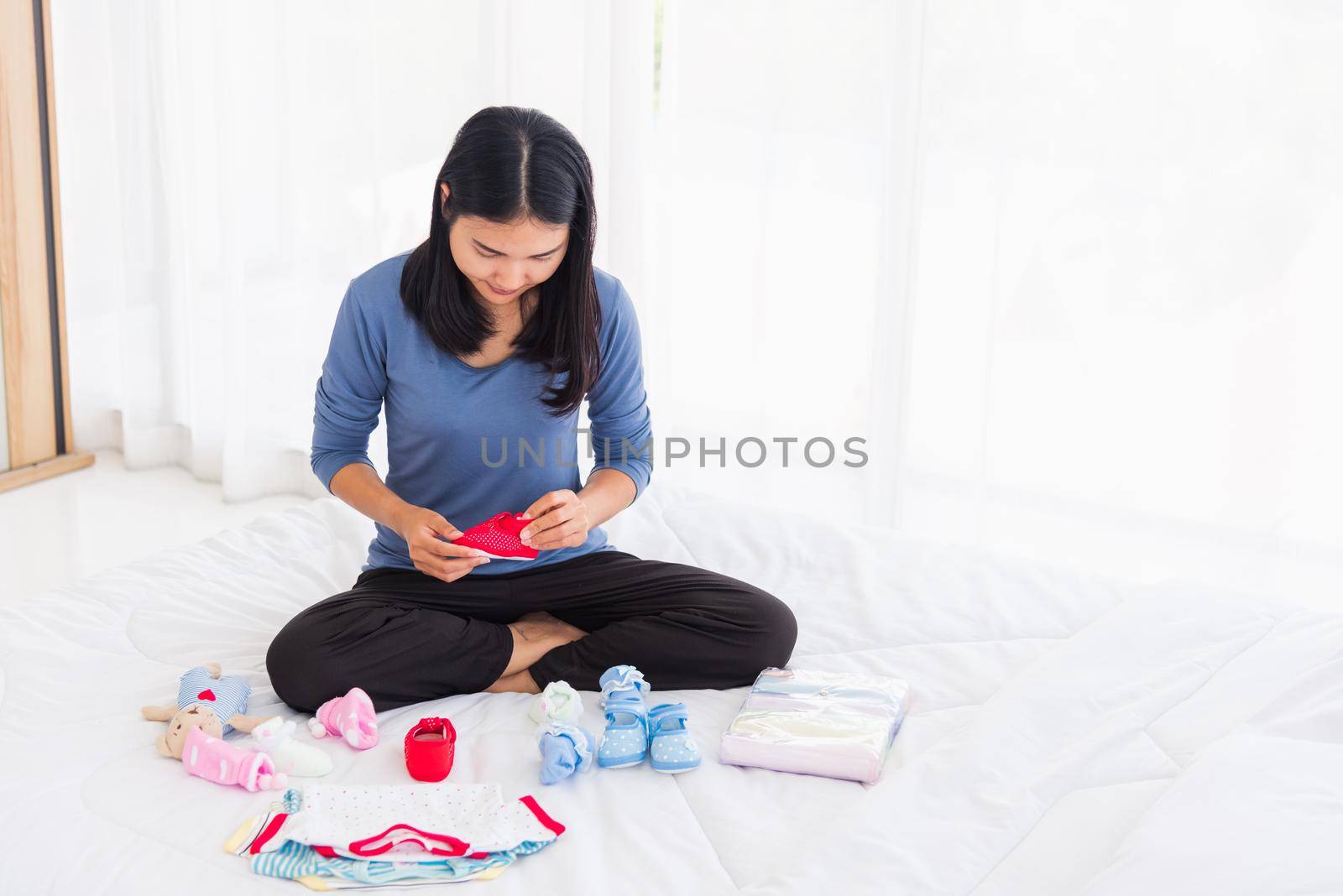 Asian mother preparing baby clothes resting and relaxing on the bed she makes purchase new baby clothes for after baby getting ready for newborn birth