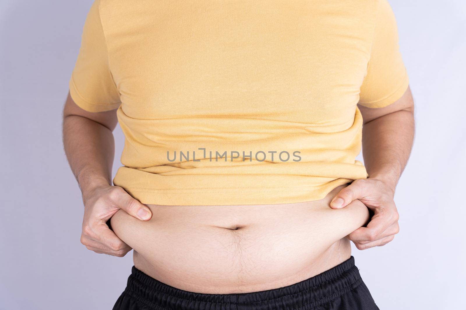 Fat man holding excessive fat belly isolated grey background.
