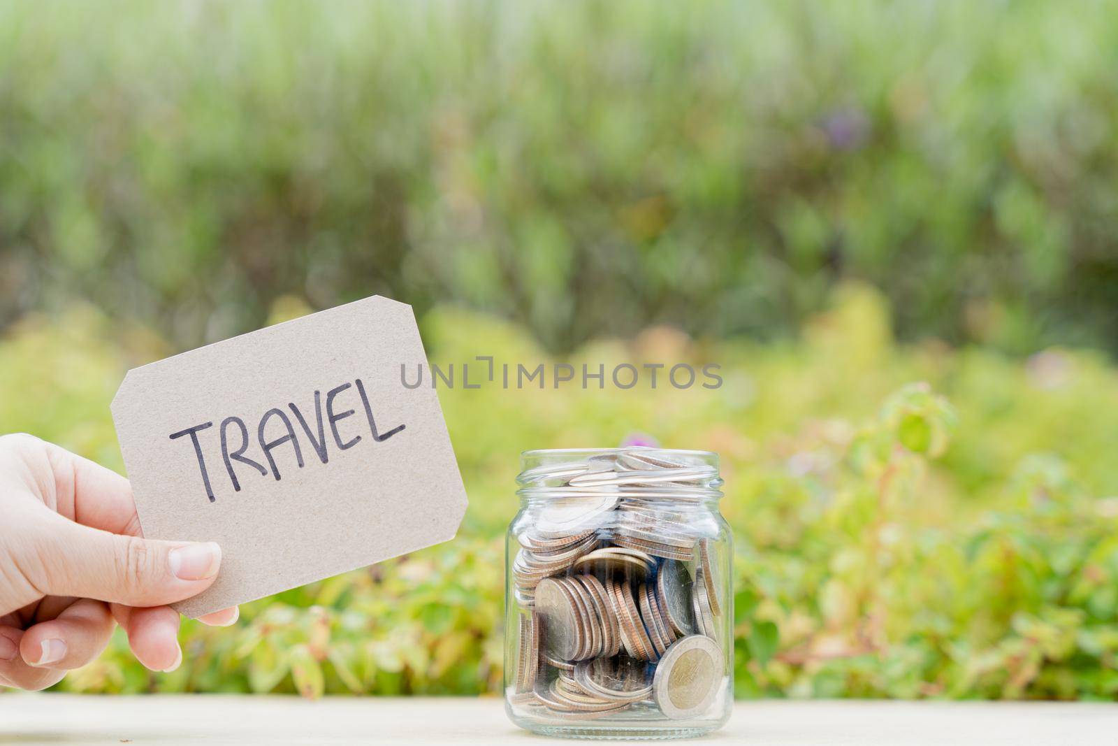 Jar full of coins with travel word paper on blurred green natural background. Saving money and investment concept. by mikesaran