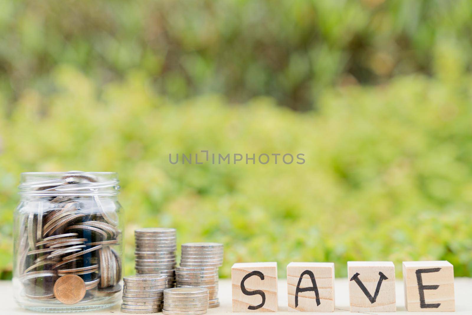 Save word on wooden block and jar full of coins on blurred green natural background. Saving money and investment concept. by mikesaran