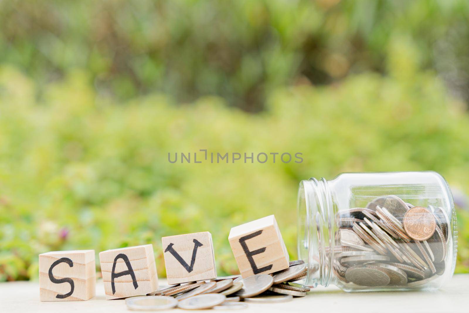 Save word on wooden block and jar full of coins on blurred green natural background. Saving money and investment concept. by mikesaran