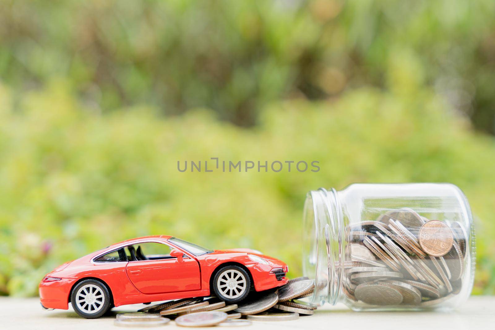 Red car on jar of coin on blurred green natural background. Saving money and investment concept. by mikesaran
