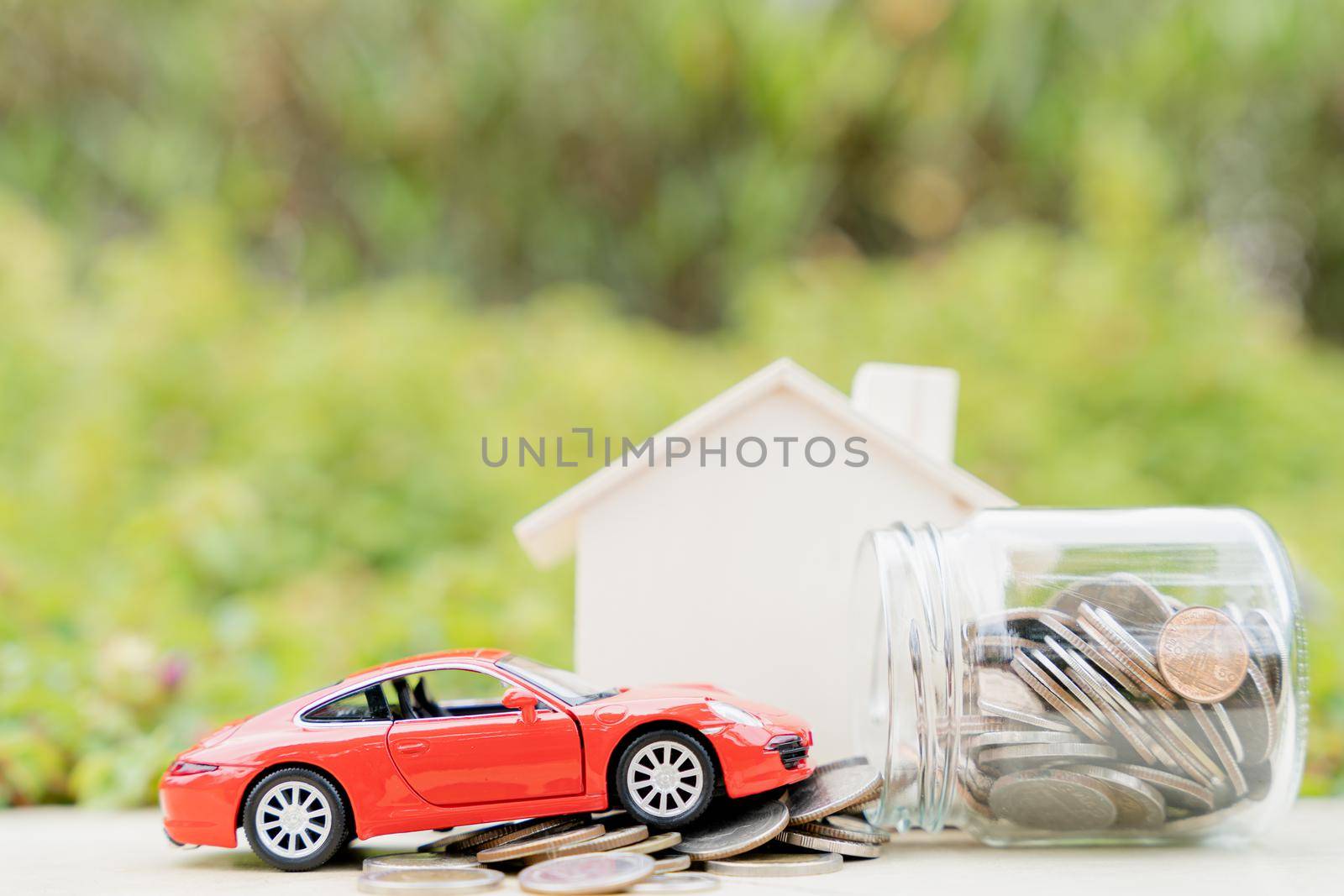 Jar of coins and red car on pile of coin on blurred green natural background. Saving money and investment concept. by mikesaran