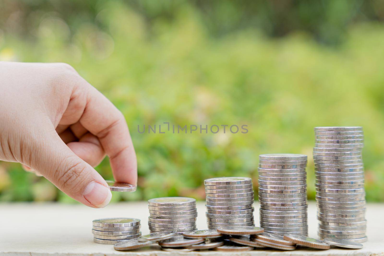 Hand put money coin on stack coins on blurred green natural background. Property investment and house mortgage financial concept.