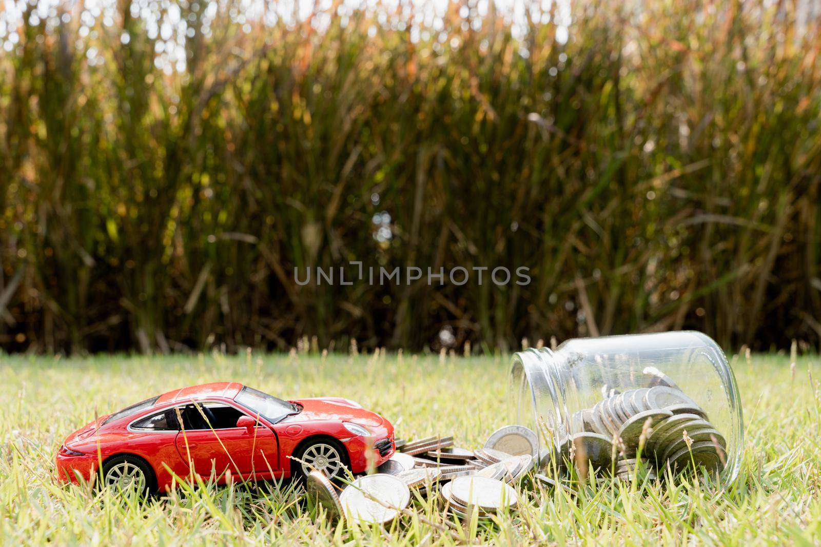 Red car on stack of coin on blurred green natural background. Saving money and investment concept. by mikesaran