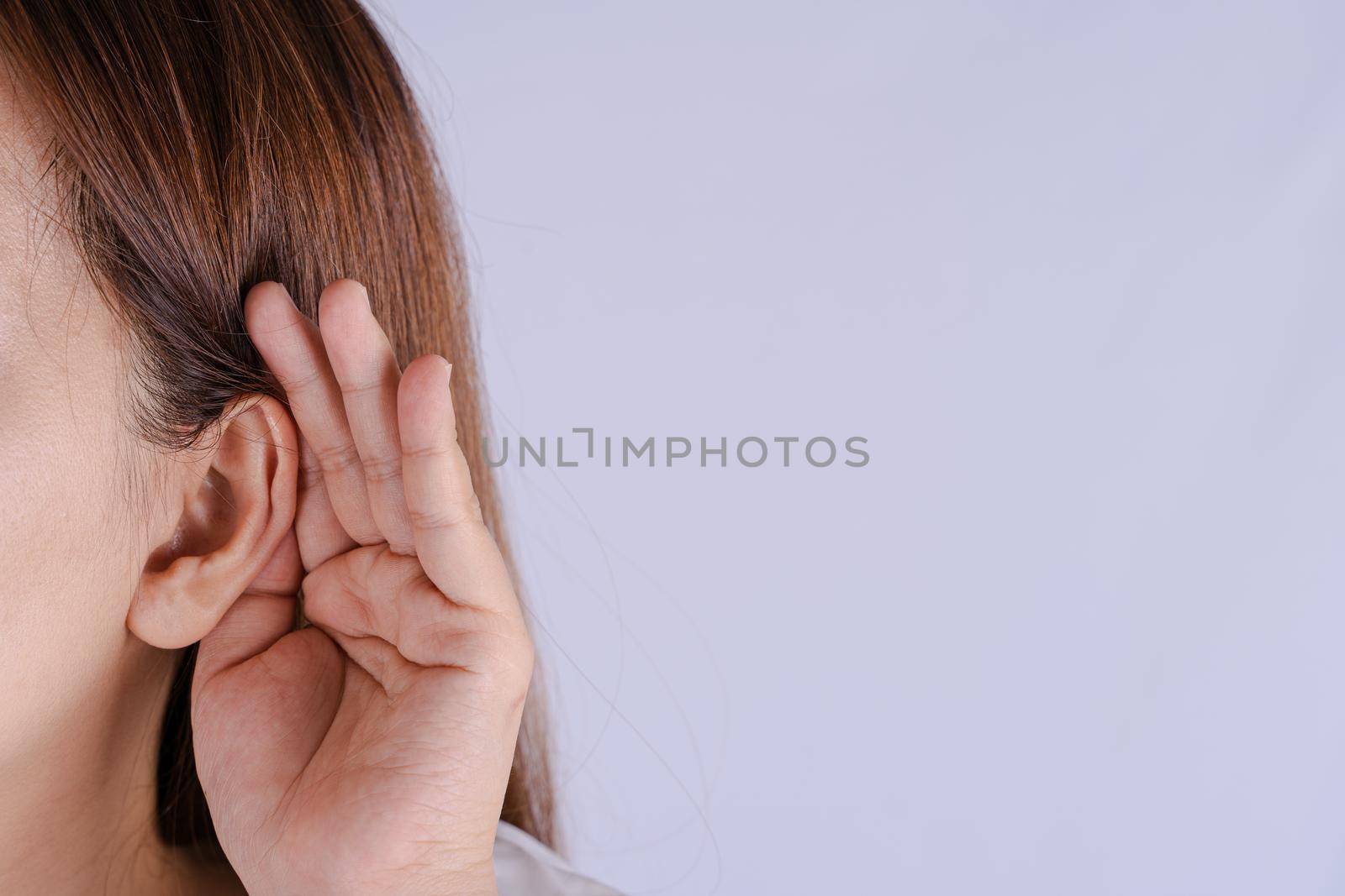woman hearing loss or hard of hearing and cupping her hand behind her ear isolate grey background, Deaf concept. by mikesaran