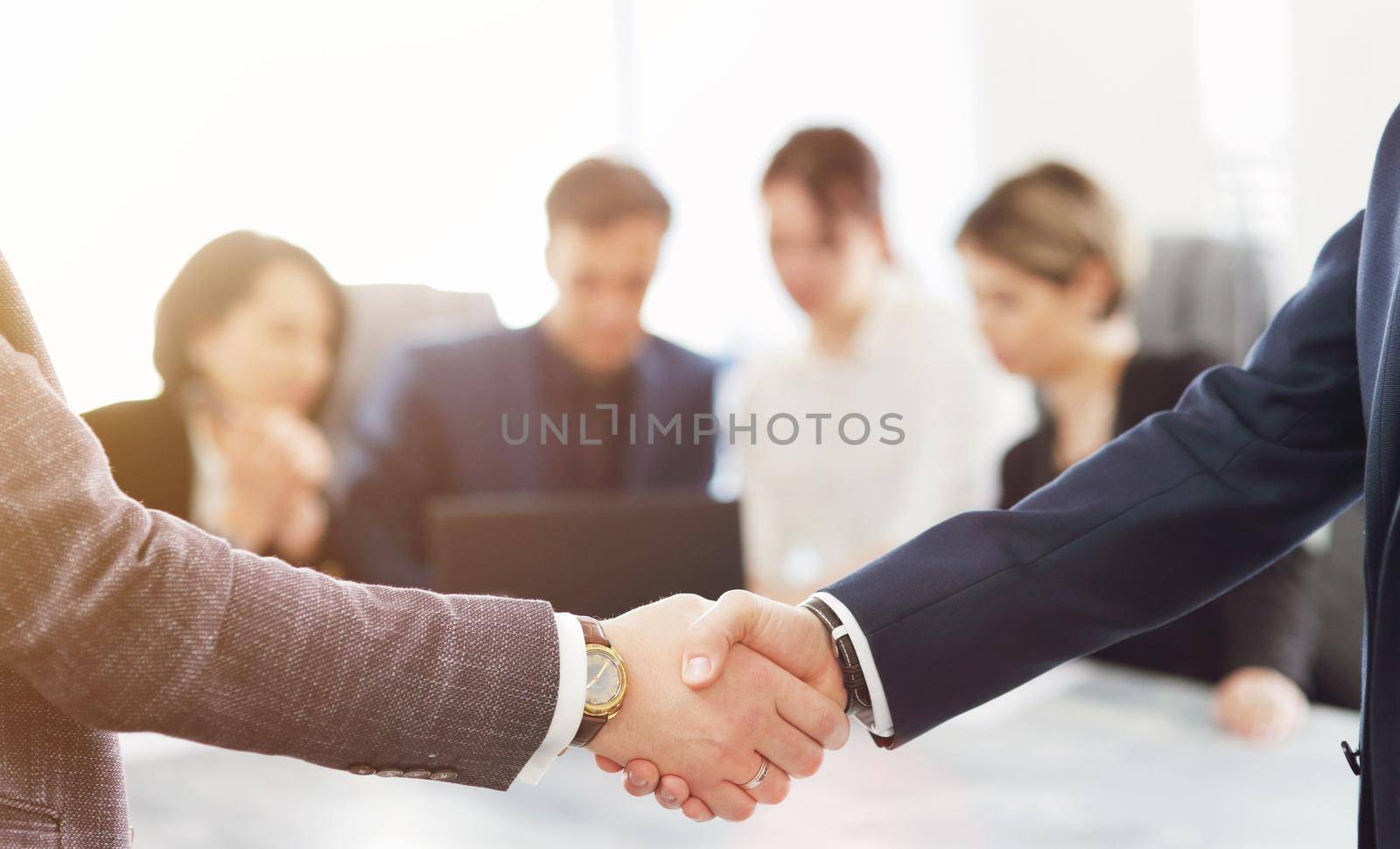Business people shaking hands finishing a meeting in the background of their work team. 