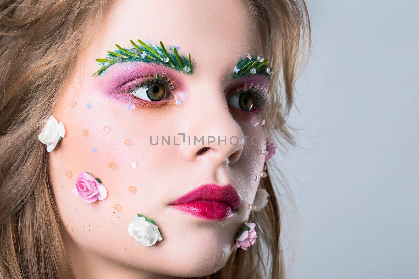 Close-up face of a beautiful girl with bright spring make-up. Summer girl in flowers. Gorgeous beauty with extended eyebrows and eyelashes. Natural cosmetics concept.